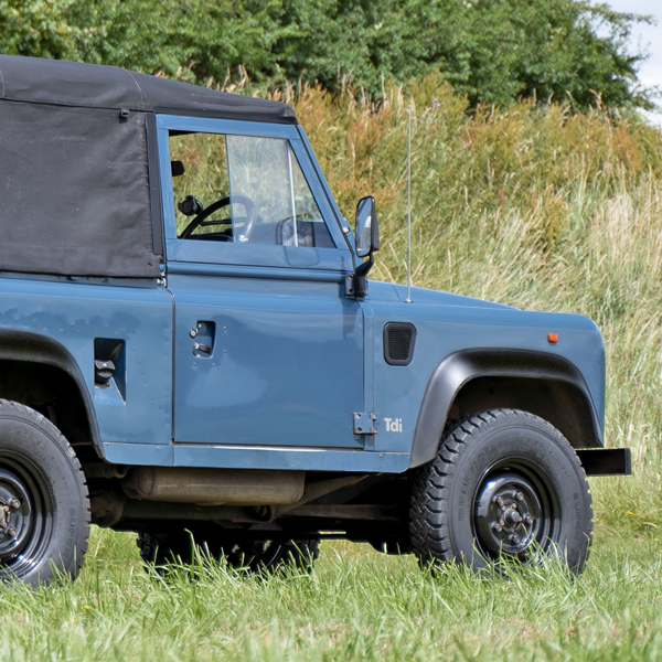 A classic blue land rover defender sat on tuff torque steel wheels in a filed.