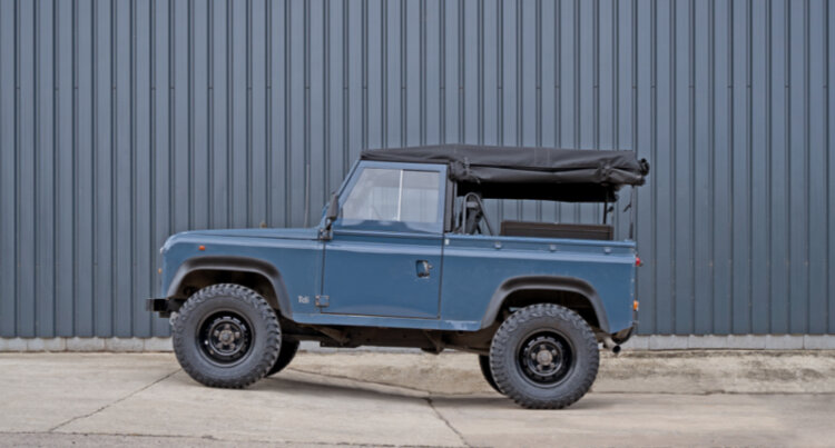 A vintage soft top land rover defender in blue sat on black steel wheels