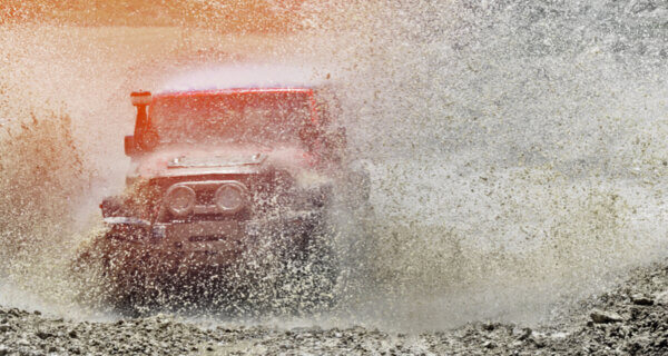 A Jeep racing through a large mud puddle sat on Mud Terrain Tyres for the Ultimate Guide to Mud Terrain Tyres